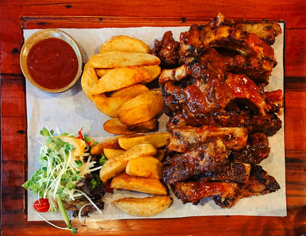 Top view of a Chicken & Ribs Family Pak with barbecue ribs, crispy potato wedges, fresh salad, and dipping sauce served on a wooden table.