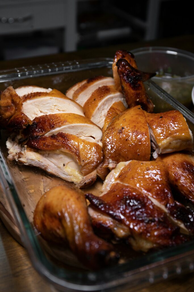 Close-up of a roasted chicken cut into portions and arranged in a glass dish, featuring juicy white meat, crispy golden-brown skin, and roasted wings.
